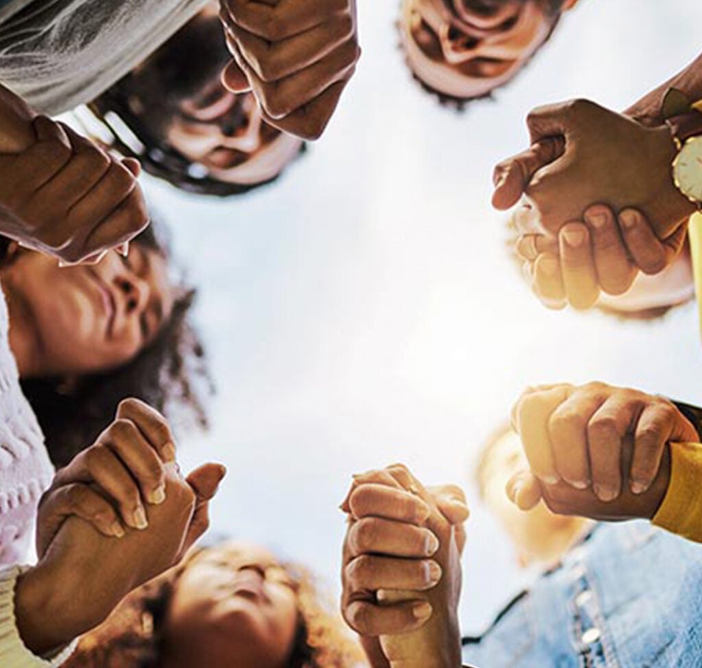 Camera angle looking up at a group of diverse people holding hands and the sun shining down on them.
